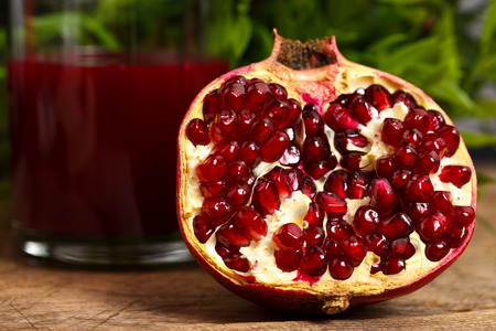 Half pomegranate on wooden table with red juice in the backの写真素材