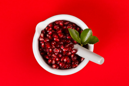 Grenadine seeds with green leaf in a porcelain mortar over red backgroundの写真素材