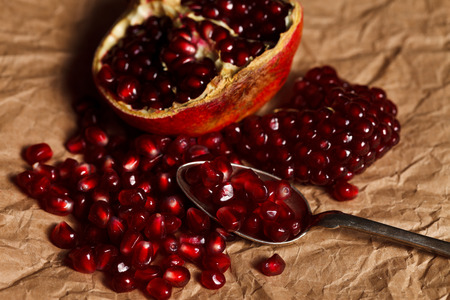 Pomegranate seeds and fruit with silver teaspoon on rustic paperの写真素材
