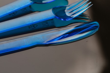 Blue plastic cutlery spoon knife fork on a dark background.の写真素材