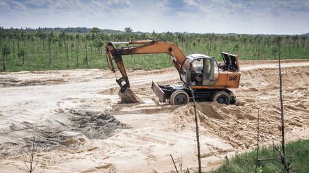 The excavator works on the consruction of the road through the swamp.