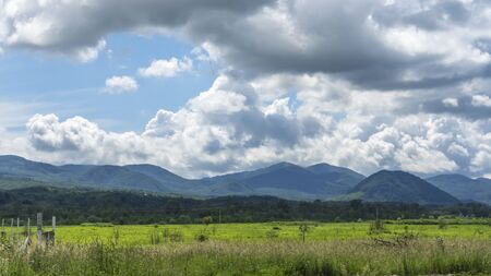 Green grass field with small mountains and dramatic sky with clouds. Travel concept.の写真素材