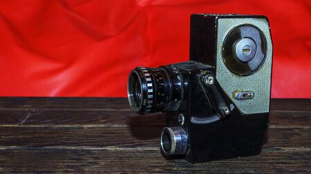 Vintage old movie camera on the wooden table on the red background. Space for text.