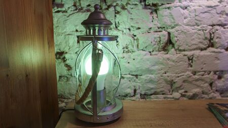 Vintage table lamp shines green light on brick wall background.