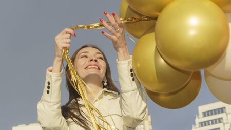 Happy young woman holding colorful balloons on the dramatic sky background. Celebration concept. Space for text.の写真素材