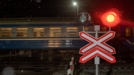 Railroad crossing with passing train by night. Train crossing gates closed on rural road at late evening. Drops of rain.の写真素材