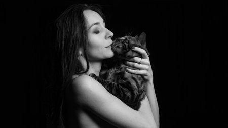 Sexy brunette caucasian woman with bengal cat in her arms on dark background.