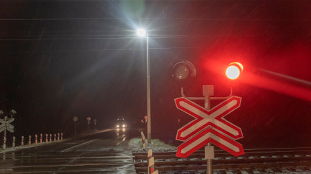Railroad crossing with passing train by night. Train crossing gates closed on rural road at late evening. Drops of rain.の写真素材