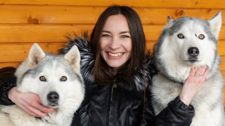 Portrait of caucasian white brunette women in black winter coat smiling next to a two gray husky...