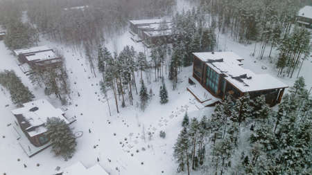 Aerial view of snow covered roofs of cottage in winter forest.