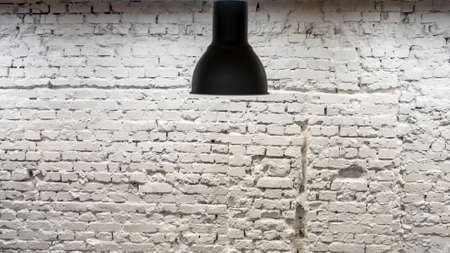 A black lamp in the interior against a white brick wall.