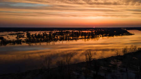 Aerial view of the setting sun beautifully illuminates cumulus clouds slowly floating over a full-flowing river on a warm spring evening. Sunset panorama over the river.の写真素材