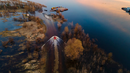 Aerial view of orange 4x4 car crossing flooded road near the river bank. Splashes and puddles on...