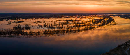 Aerial view of the setting sun beautifully illuminates cumulus clouds slowly floating over a full-flowing river on a warm spring evening. Sunset panorama over the river.の写真素材