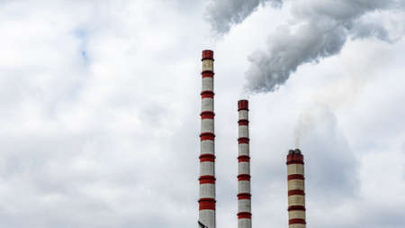 Industrial smoke from chimney on dramatic sky background. View of high chimney pipes with gray smoke...