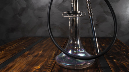 Modern hookah with glass bowl on wooden table. Gray wall background.