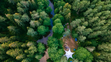 Top view camping in the holidays. Tourist tents in the forest on the river bank. Aerial view.