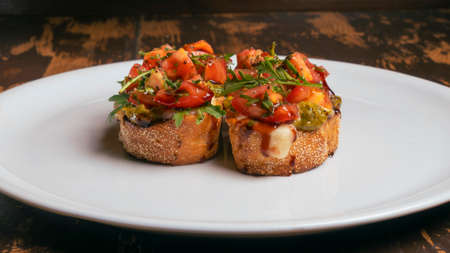 Close-up view of tomato and mozzarella bruschetta on white plate on red brick wall background.