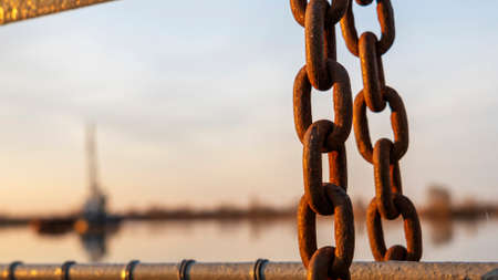 The old chain by the pier at sunset. Defocused background with ship and dramatic sky. Space for...