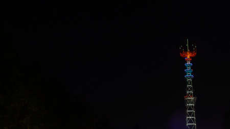Glowing TV tower at night. Festive illuminated broadcast tower. Space for text.