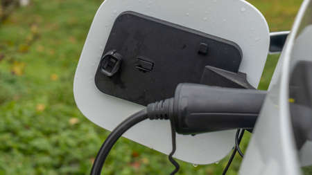 White electric car is charged in the village. Private electric car charger. Electric charge in a...
