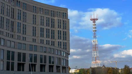 A TV tower on the background of a blue sky with clouds. Near a modern office building. Space for...