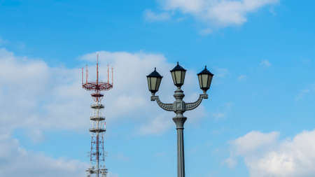 A TV tower on the background of a blue sky with clouds. In the foreground is a vintage street lamp. History tellecommunication concept. Space for text.の写真素材
