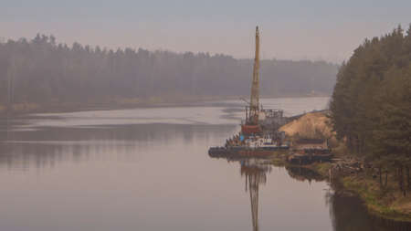 Floating crane on the river. Dredging crane working near shore. Conservation river flow. Nature, river, sky, clouds. Cleaning the bottom of the river.の写真素材