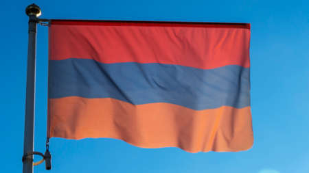 Part of the flag of Armenia with alternative colors on the flagpole waving in the wind on a blue...