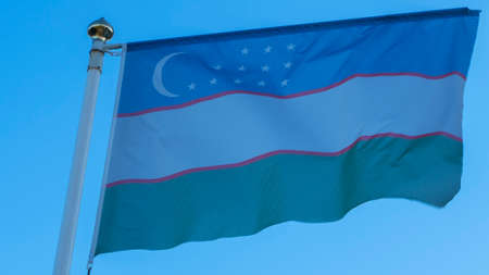 National flag of Uzbekistan on a flagpole in front of blue sky with sun rays and lens flare. Diplomacy concept. International relations. Space for text.の写真素材