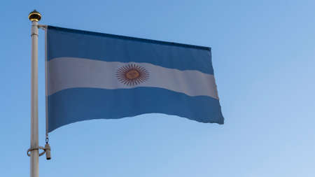 National flag of Argentina on a flagpole in front of blue sky with sun rays and lens flare. Diplomacy concept.の写真素材