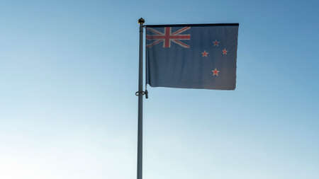 National flag of New Zealand on a flagpole in front of blue sky with sun rays and lens flare. Diplomacy concept.の写真素材