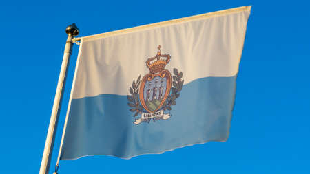National flag of San Marino on a flagpole in front of blue sky with sun rays and lens flare. Diplomacy concept. International relations. Space for text.の写真素材