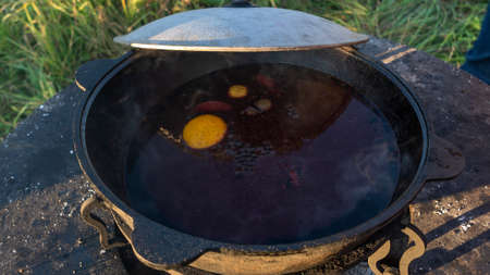 Mulled wine in a large cauldron. Mulled wine is cooked in a large pot. Vitamins in the traditional festival. Mulled wine on fire with various fruits and spicesの写真素材