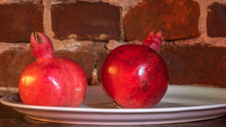 Two fruit juicy Spanish pomegranate on porcelain plate on a red brick wall background. Healthy life concepts.の写真素材