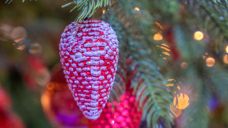 Traditional artificial Christmas tree with Christmas red cone toy and glowing colorful lights in background. Xmas concepts. Close-up of Christmas tree. Defocused background.の写真素材