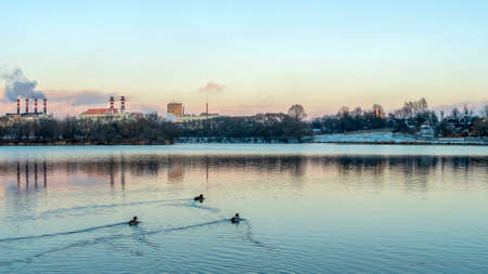 Smoking chimneys of thermal power plants near the waterfront in city. Winter. Industrial and nature...