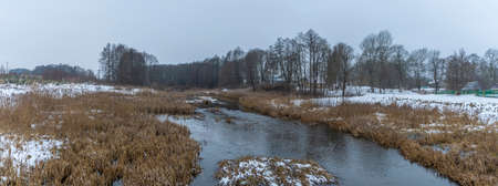 Winter landscape of a small river in early winter on a cloudy day. River dry grass in the crystals. Water stream flowing in a field in winter.の写真素材