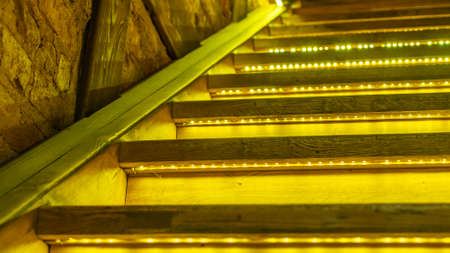 Yellow led light pouring from below onto a wooden staircase. Space for text. Abstract background. Image for design.の写真素材