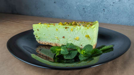 Close-up view of green pistachio cake with leaf of mint on black plate. Creamy pistachio cheesecake. Festive concepts.の写真素材