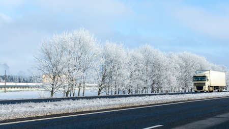 Truck goes on winter road. Van in the road of winter. Lorry car and cold landscape. Roadway and route snowy street trip. Winter road transportation truck. Logistic concepts.の写真素材