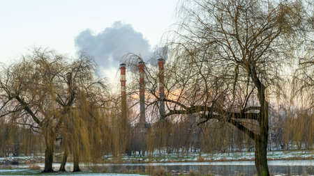 Industrial air pollution. Winter landscape with factory and trees. The concept of environmental pollution. A factory with a pipe releasing smoke on the background.の写真素材