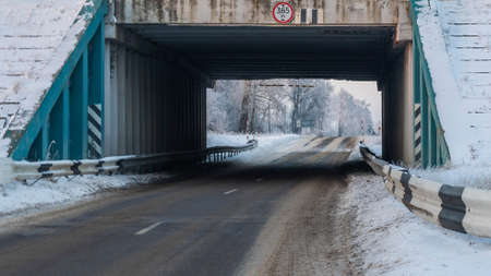 Outdoor scenery of empty street pass through small tunnel under highway and agriculture field covered by snow in winter. Space for text.の写真素材