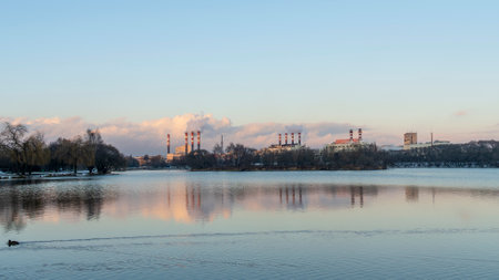 Smoking chimneys of a thermal power plant against a winter cloudy sky. environmental problems concept. Space for text. Panoramic view of the lake with power station in the background.の写真素材