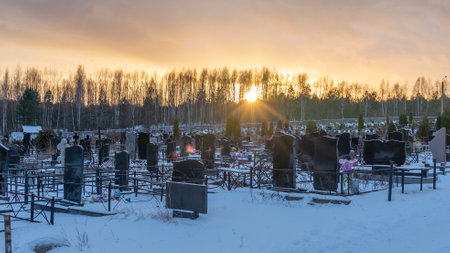 Winter sunset over a snow covered cemetery with dark headstones and trees. Afterlife. Samsara concepts.の写真素材