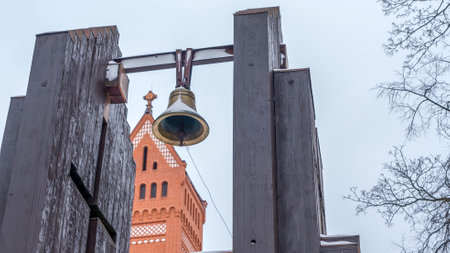 Church over cloudy grey sky. Belfry with a bell against the background of a red church. Worship concepts.の写真素材