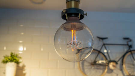 Efficient incandescent light bulb waste electricity against a tiled wall with a small bike and a plant pot. Decorative antique edison light bulb. Space for text.の写真素材