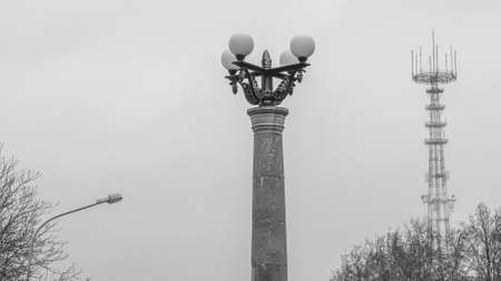 Black and white image of a massive old street lamp with a TV tower and the winter gray sky in the background. The concept of loneliness and reflection. Winter urban background. Space for text.の写真素材