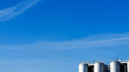 Part of steel tanks of silvery color on a background of the blue sky. Space for text. Winery or petroleum concepts. Series of stainless steel containers for wine.の写真素材