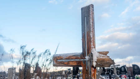 Snowy old broken grave wooden cross shaped on dramatic sky background. Orthodox traditional cemetery in snowy winter. Space for text.の写真素材